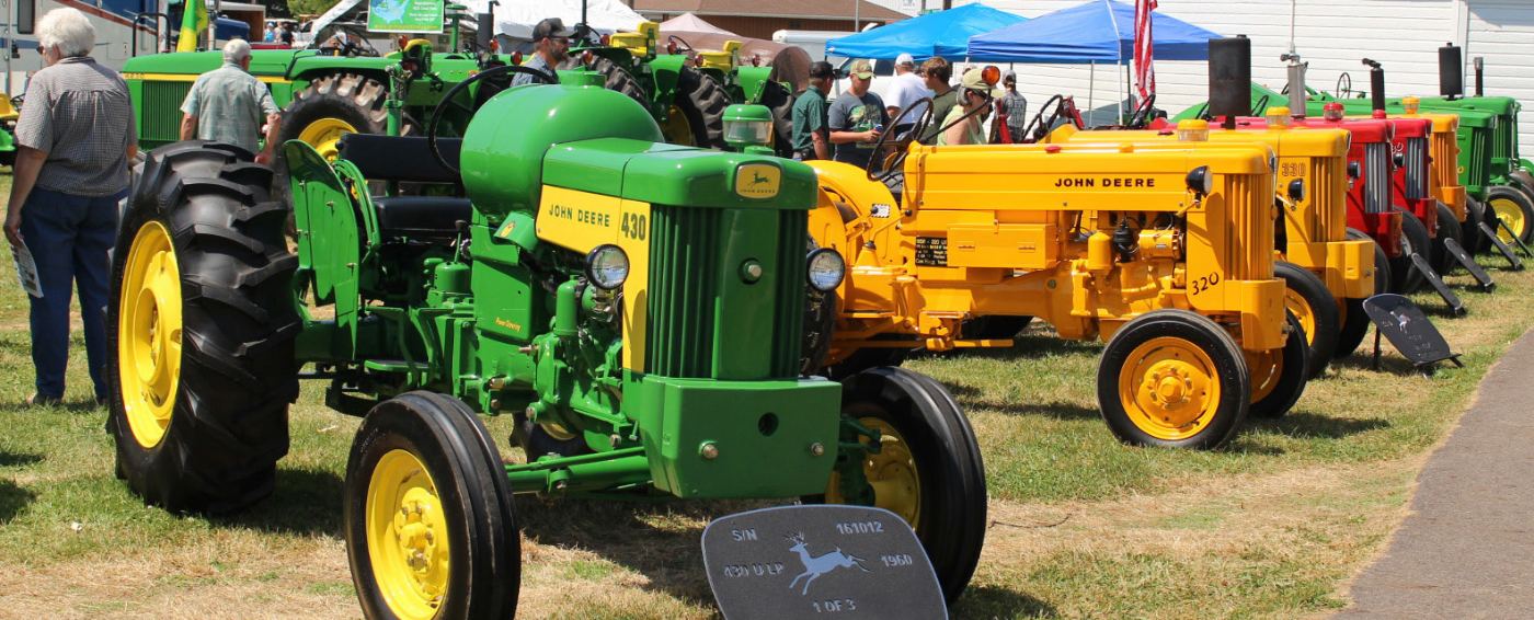 A John Deere 430 leads a row of yellow and red commercial 320 and 330 tractors