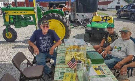 Club members seated at a ticket table beside John Deere tractors