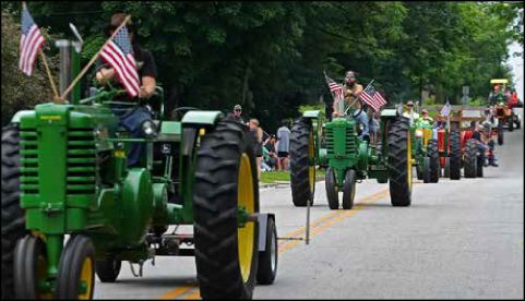 Line of John Deere tractors with American flags in a street parade