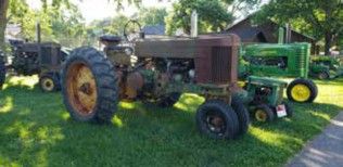Unrestored John Deere tractors parked in the shade