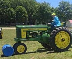 Driver on a John Deere tractor beside a blue barrel