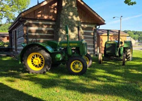 Two early John Deere tractors beside a log cabin